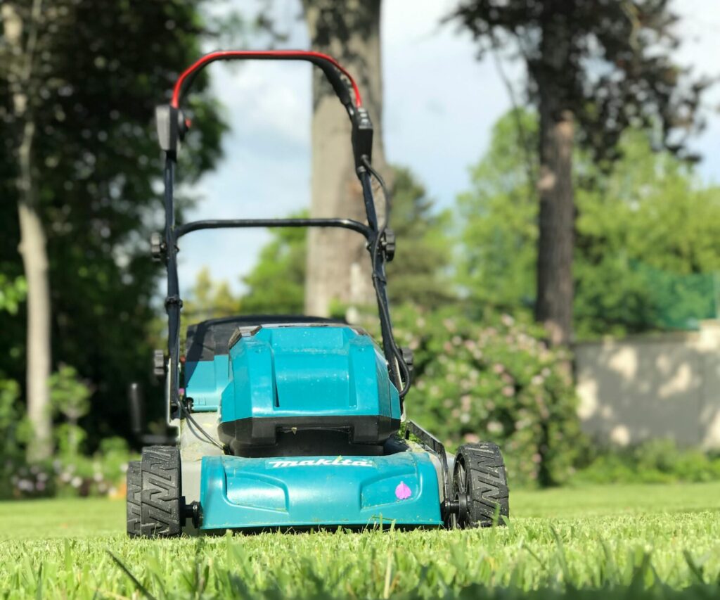 A blue lawn mower on a lush green lawn during a sunny summer day in Göd, Hungary.