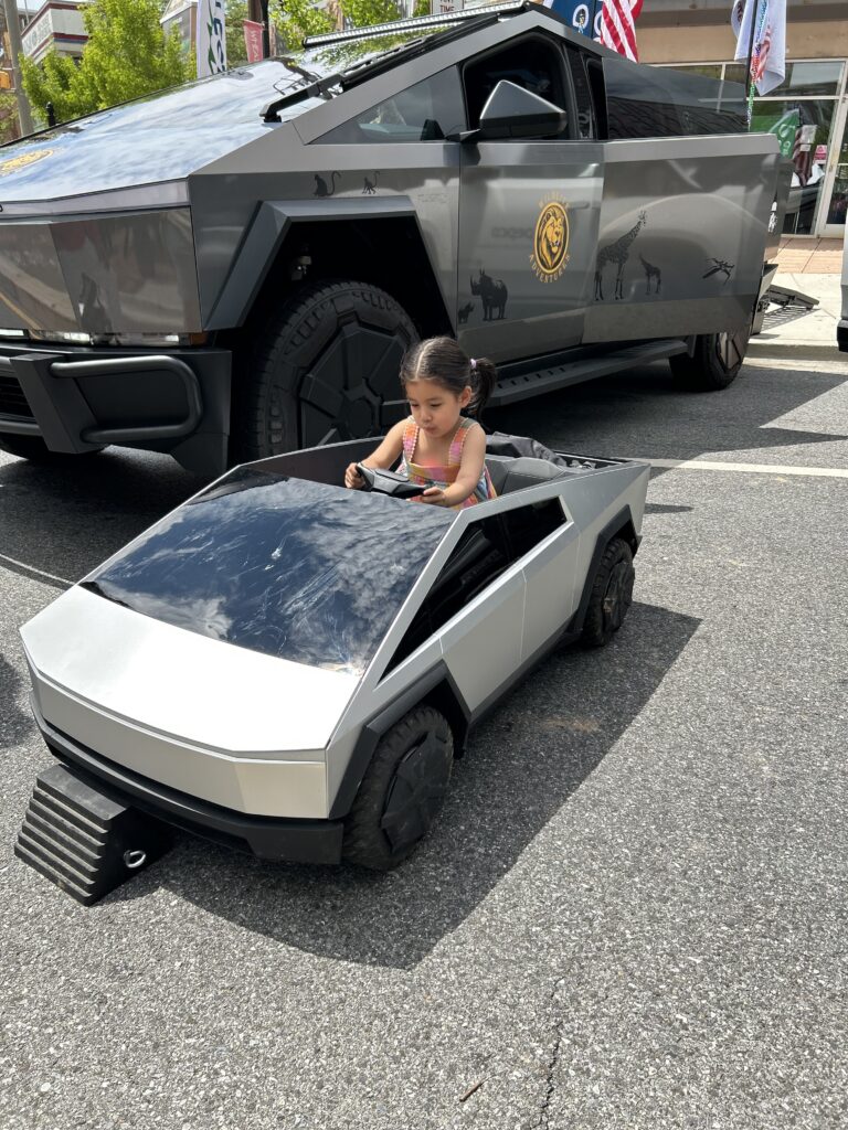 mini tesla truck with child in it alongside a full size tesla truck