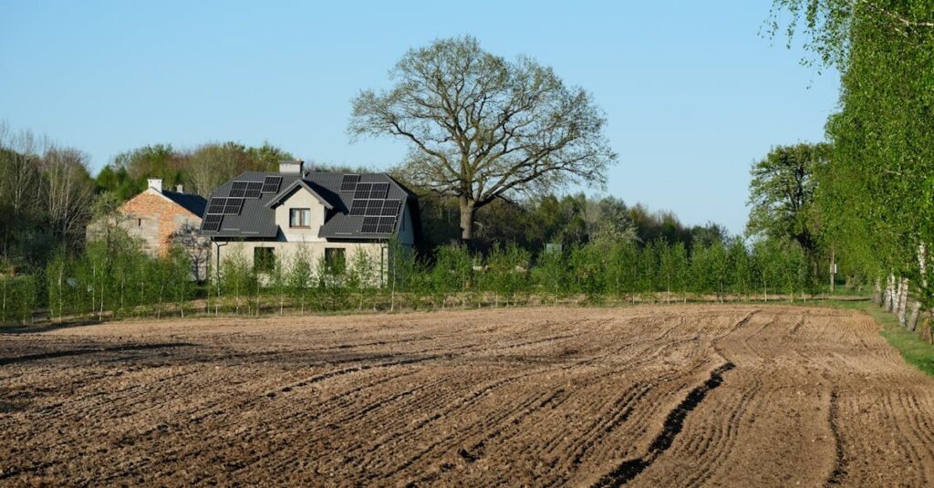 Rural house with solar panels surrounded by farmland and trees.