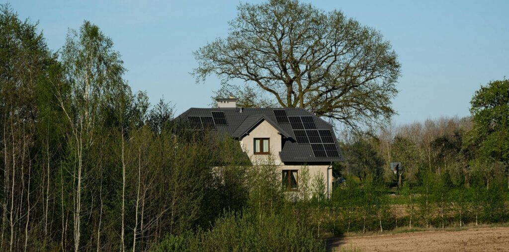 Modern house with solar panels surrounded by lush trees and fields, embracing sustainable living.